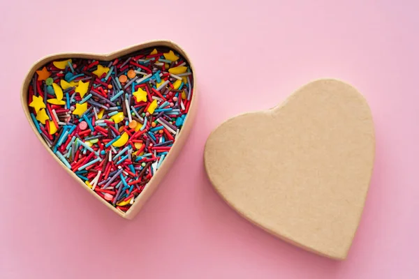 Top view of colorful sprinkles in heart shaped box on pink background — Stock Photo