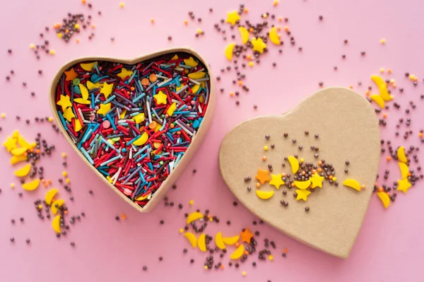Vista superior de salpicaduras dulces en caja de regalo en forma de corazón sobre fondo rosa - foto de stock