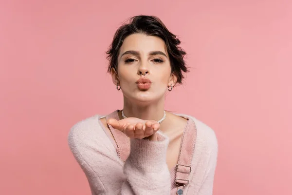Pretty brunette woman in cozy cardigan sending air kiss and looking at camera isolated on pink — Stock Photo