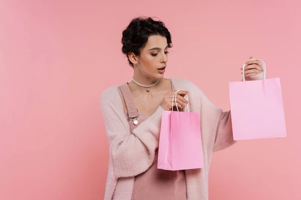 Étonnante jeune femme dans un cardigan moelleux tenant des sacs à provisions isolés sur rose — Photo de stock