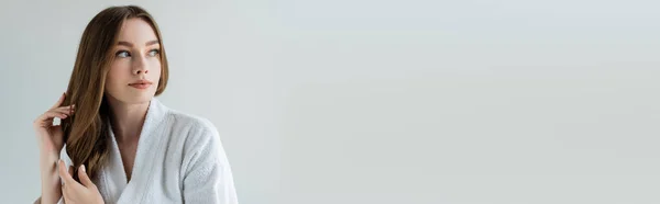 Young woman with shiny and healthy hair looking away isolated on grey, banner — Stock Photo