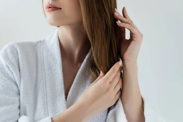 Vista recortada de mujer joven tocando pelo brillante y saludable aislado en gris - foto de stock