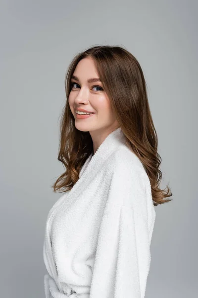 Lächelnde junge Frau mit glänzendem und gesundem Haar, während sie in die Kamera schaut, isoliert auf grau — Stockfoto