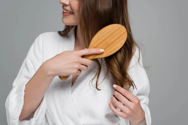 Vista cortada da jovem mulher alegre escovando cabelo brilhante e saudável isolado no cinza — Fotografia de Stock