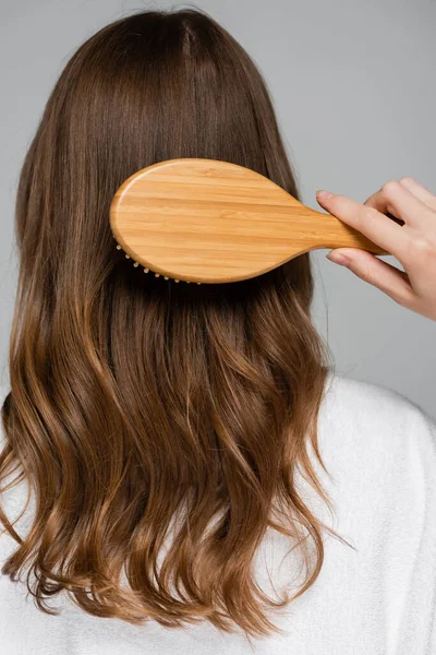 Back view of young woman brushing shiny and healthy hair isolated on grey — Stock Photo