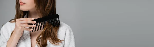 Visão parcial da jovem escovação cabelo brilhante com pente de plástico isolado em cinza, banner — Fotografia de Stock