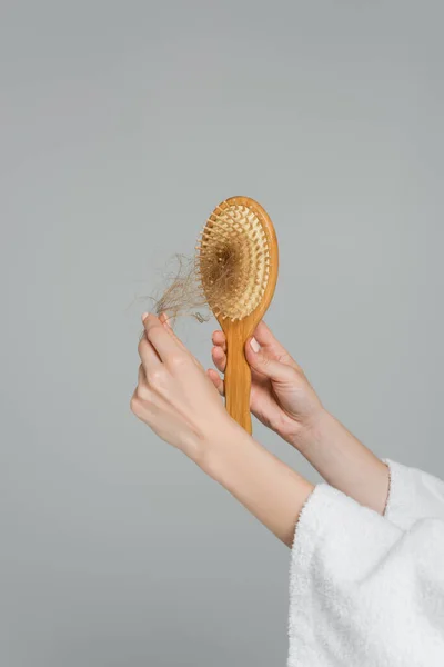 Visão parcial da jovem segurando escova de cabelo de madeira e puxando o cabelo danificado isolado no cinza — Fotografia de Stock