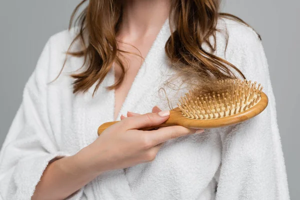 Vista parziale di giovane donna in possesso di spazzola per capelli in legno con capelli danneggiati isolati su grigio — Foto stock