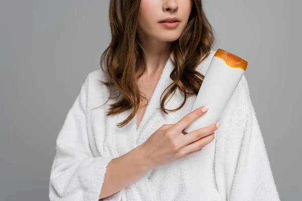 Cropped view of young woman with shiny hair holding bottle with shampoo isolated on grey — Stock Photo