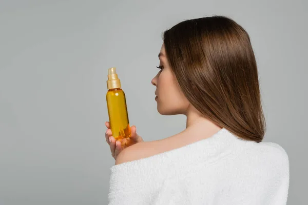 Vista posteriore della giovane donna con bottiglia di capelli lucidi con olio isolato su grigio — Foto stock