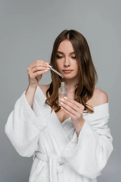 Pretty young woman with shiny hair holding bottle and pipette with serum isolated on grey — Stock Photo