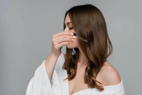Young woman applying serum on shiny hair isolated on grey — Stock Photo