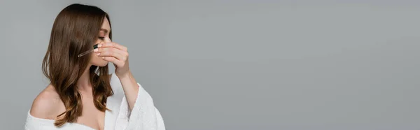 Young woman applying serum on shiny hair isolated on grey, banner — Stock Photo