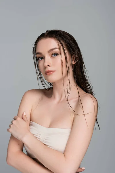 Pretty and young woman with wet hair and bare shoulders looking at camera isolated on grey — Stock Photo