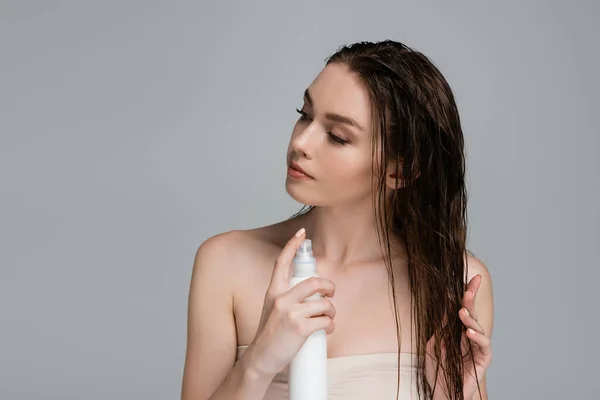 Jolie jeune femme aux épaules nues appliquant produit de traitement sur cheveux mouillés isolé sur gris — Photo de stock