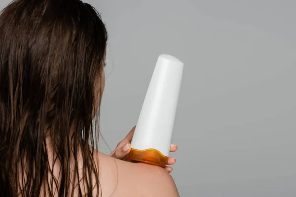 Vue arrière de la jeune femme aux cheveux mouillés tenant bouteille avec shampooing isolé sur gris — Photo de stock