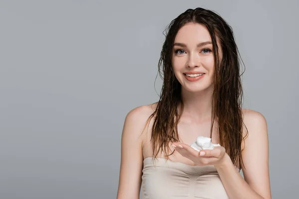 Young and cheerful woman with wet hair holding foam in hand isolated on grey — Stock Photo