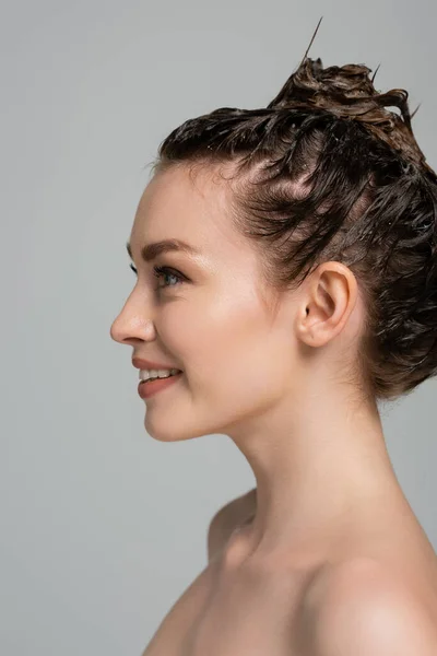 Alegre joven con espuma en la cabeza mirando hacia otro lado mientras lava el cabello aislado en gris - foto de stock