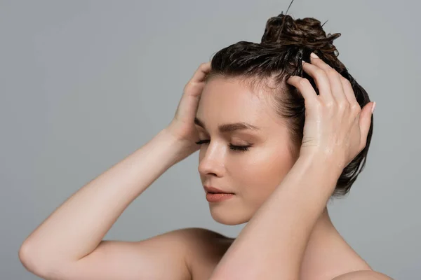 Jeune femme aux yeux fermés lavant les cheveux isolés sur gris — Photo de stock