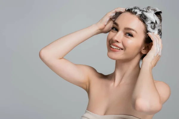 Fröhliche junge Frau wäscht nasses und schäumendes Haar isoliert auf grau — Stockfoto