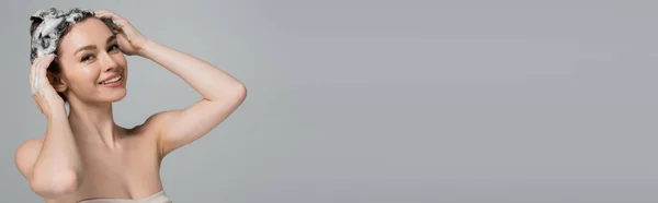 Cheerful young woman washing wet and foamy hair isolated on grey, banner — Stock Photo