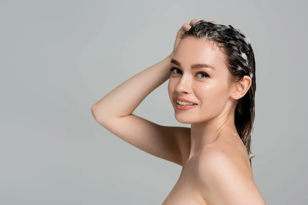 Joyful young woman washing wet and foamy hair isolated on grey — Stock Photo