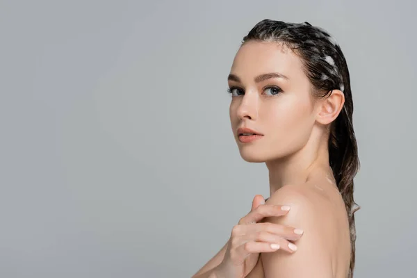 Young woman with foamy and wet hair touching bare shoulder isolated on grey — Stock Photo