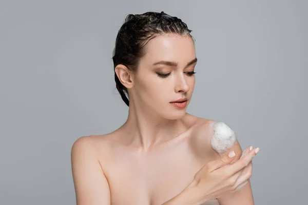 Young woman with wet hair touching bare shoulder with white foam isolated on grey — Stock Photo