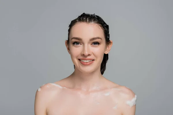 Feliz joven con el pelo mojado y los hombros desnudos sonriendo aislado en gris - foto de stock