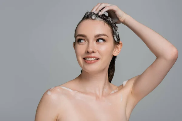 Cheerful young woman washing foamy hair isolated on grey — Stock Photo