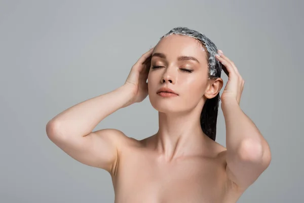 Young woman with closed eyes applying mask on wet hair isolated on grey — Stock Photo