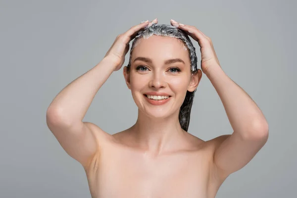 Heureuse jeune femme aux épaules nues appliquant masque sur cheveux mouillés isolé sur gris — Photo de stock