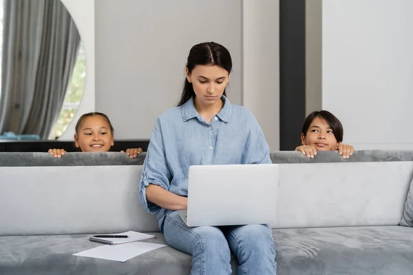 Asiático crianças olhando para a mãe usando laptop perto notebook no sofá em casa — Fotografia de Stock