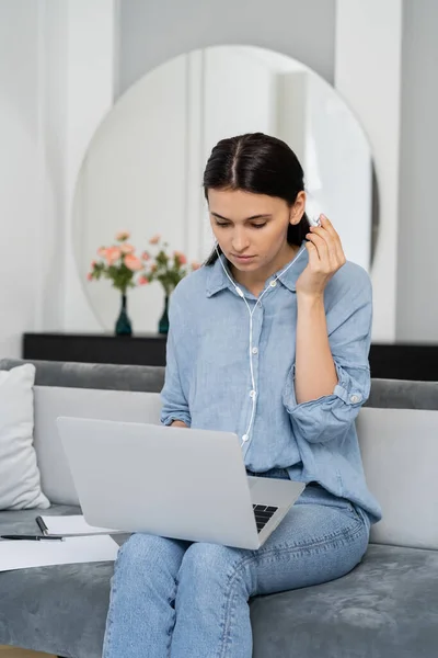 Brunette freelancer using earphones while working on laptop in living room — Stock Photo