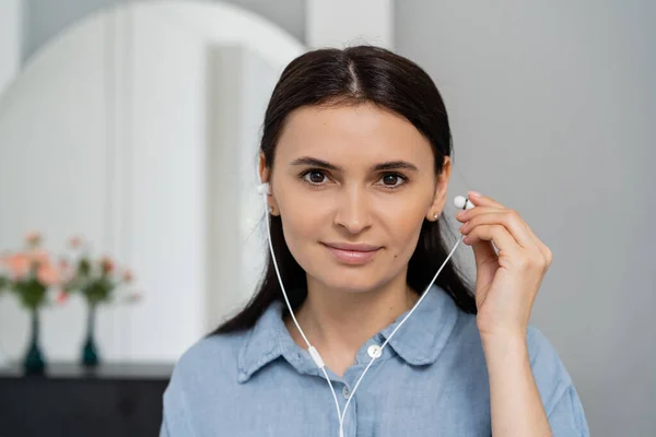 Portrait of brunette woman using earphones and looking at camera at home — Stock Photo