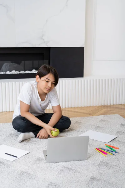 Preteen asiatico ragazzo holding apple vicino laptop e colore matite a casa — Foto stock
