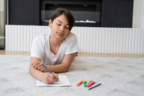 Азиатский мальчик с цветным карандашом рисунок на бумаге на полу дома — стоковое фото