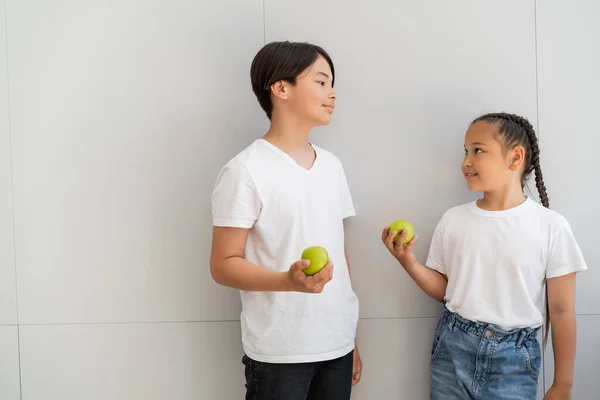 Souriant asiatique enfants tenant des pommes près du mur à la maison — Photo de stock