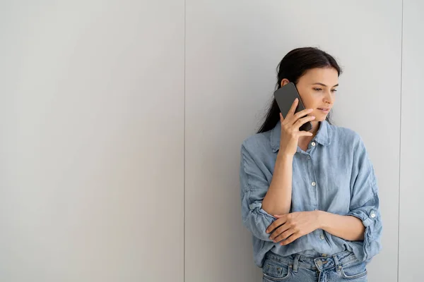 Жінка з Брюнета розмовляє на смартфоні біля сірої стіни вдома. — Stock Photo