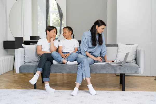 Cheerful asian kids talking while mother working on laptop at home — Stock Photo
