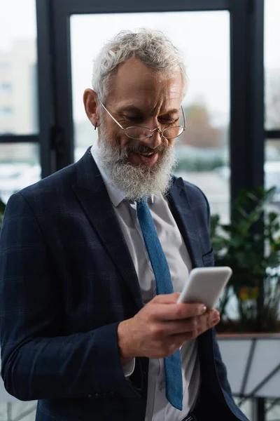 Positive businessman in suit using mobile phone in office — Stock Photo
