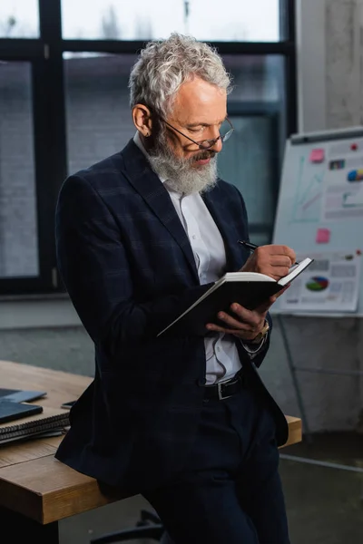 Mature businessman in suit writing on notebook in office — Stock Photo