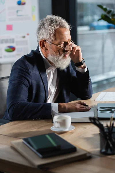 Grey haired businessman working with laptop and notebook in office in evening — Stock Photo