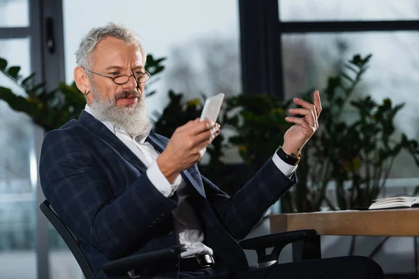 Mature manager in eyeglasses using smartphone in office in evening — Stock Photo