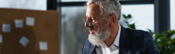 Grey haired manager in suit and eyeglasses working in office in evening, banner — Stock Photo