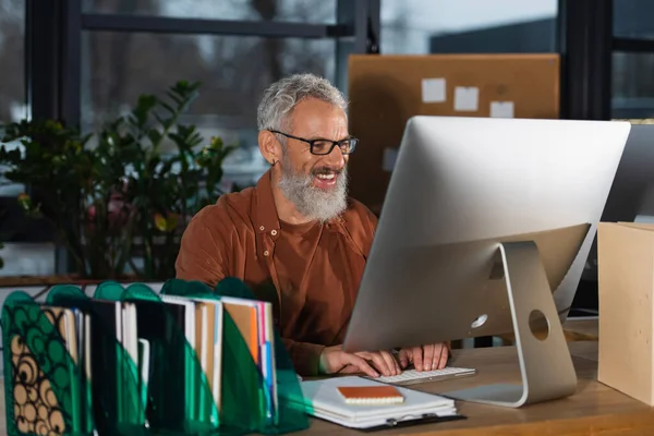 Positive businessman using computer near documents in office in evening — Stock Photo