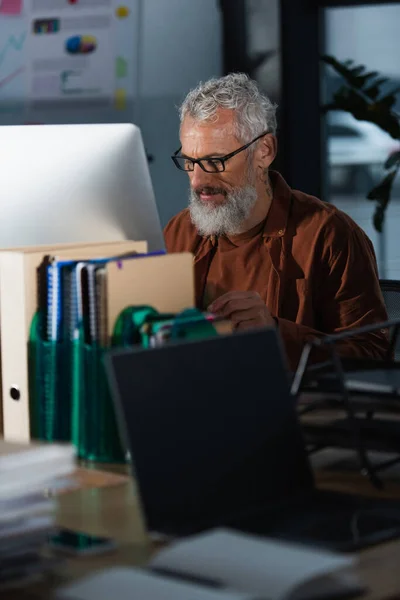 Grey haired businessman working near computer and documents in office — Stock Photo
