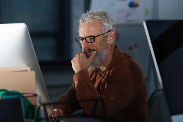 Focused businessman in eyeglasses using computer in office in evening — Stock Photo