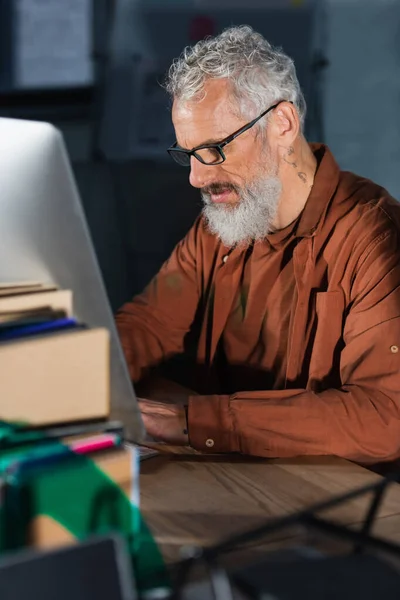 Middle aged businessman in eyeglasses using computer in office in evening — Stock Photo