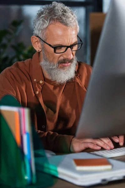 Homme d'affaires d'âge moyen utilisant un ordinateur près de documents flous dans le bureau — Photo de stock